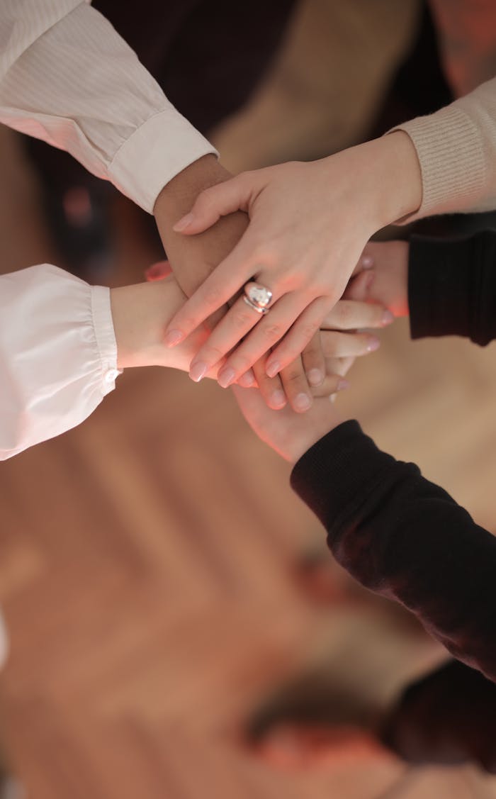 Contact Top view of faceless friends in different clothes stacking hands together while standing on wooden floor indoor on sunny day