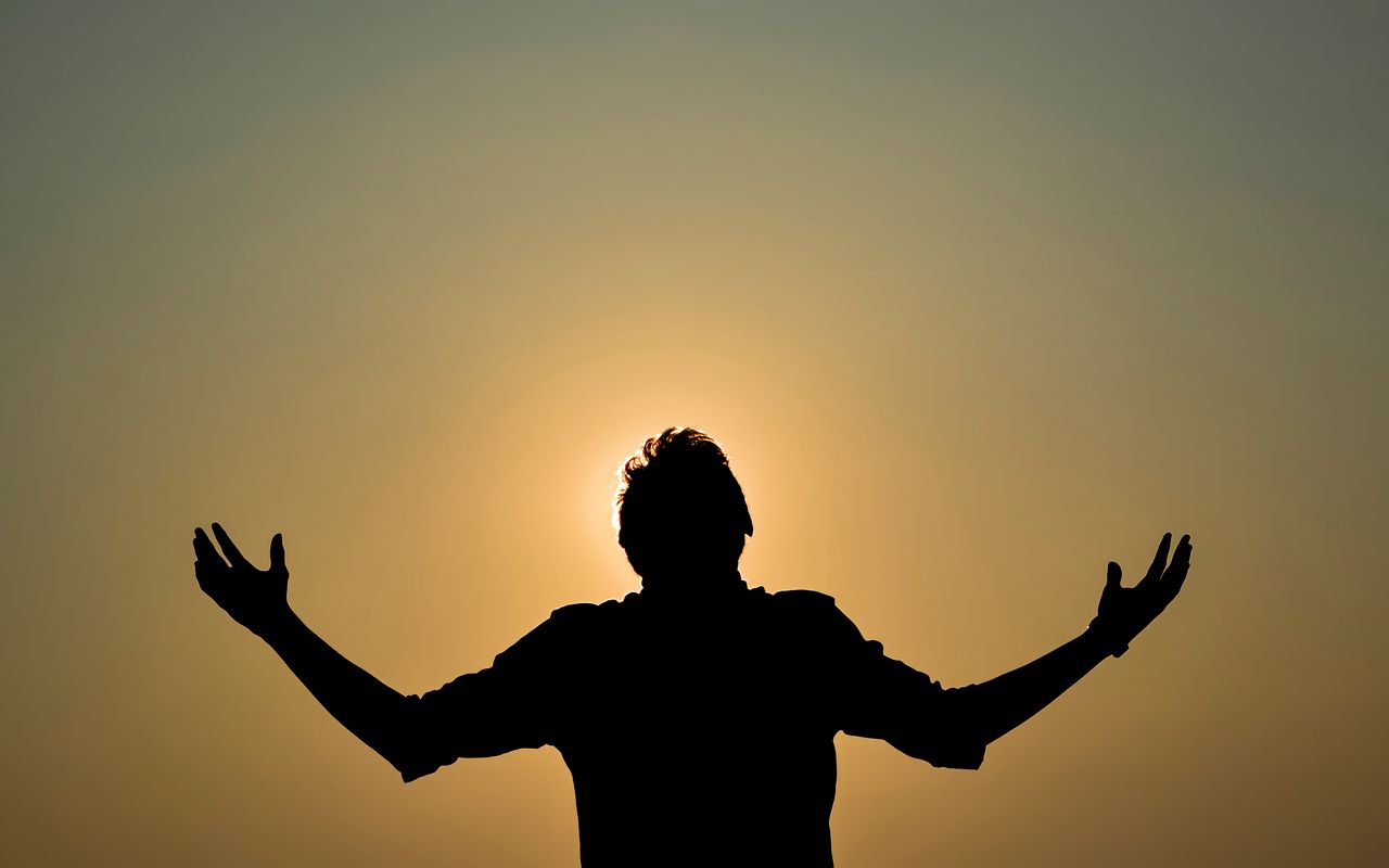 Home Captivating silhouette of a man with raised hands against a golden sky during sunset, capturing a dramatic moment.