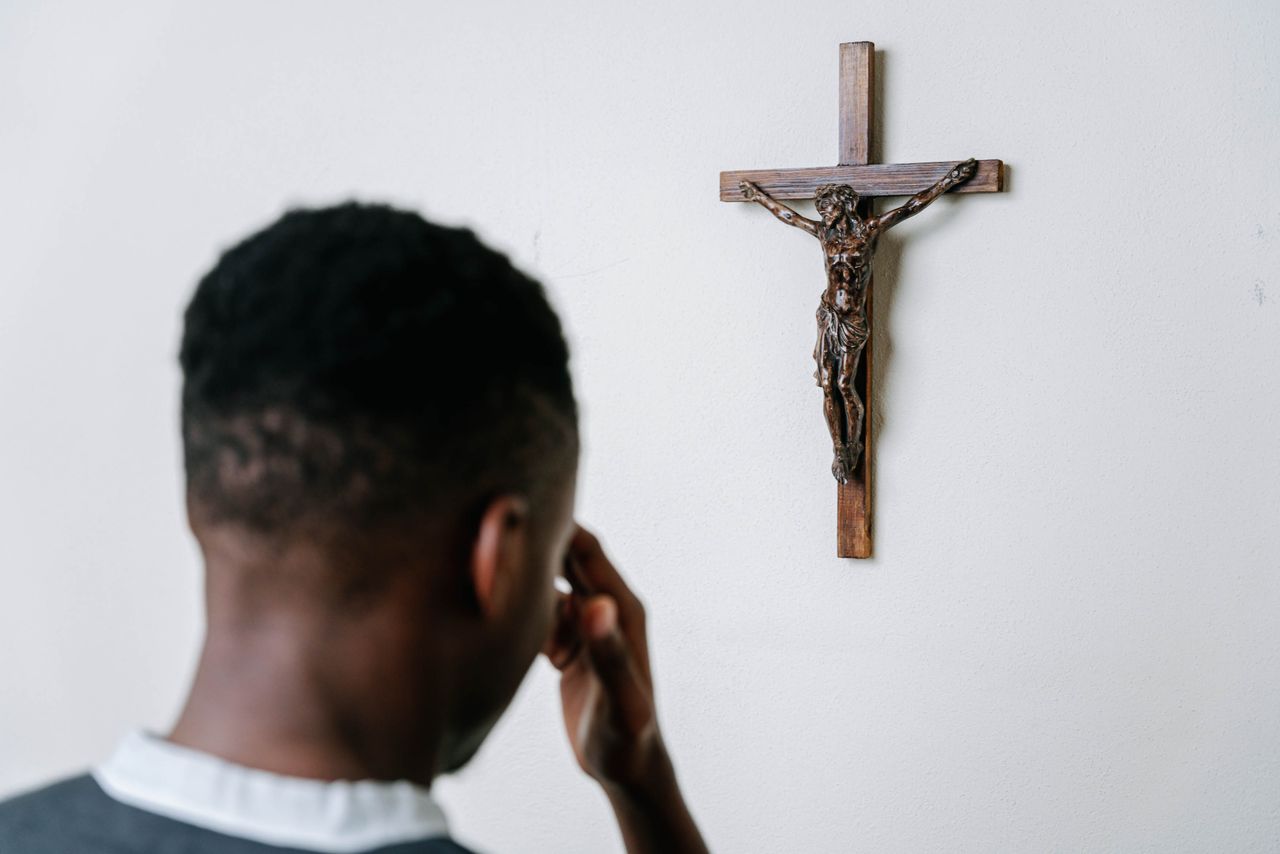 About A person praying before a wooden crucifix on a plain wall, symbolizing faith and devotion.